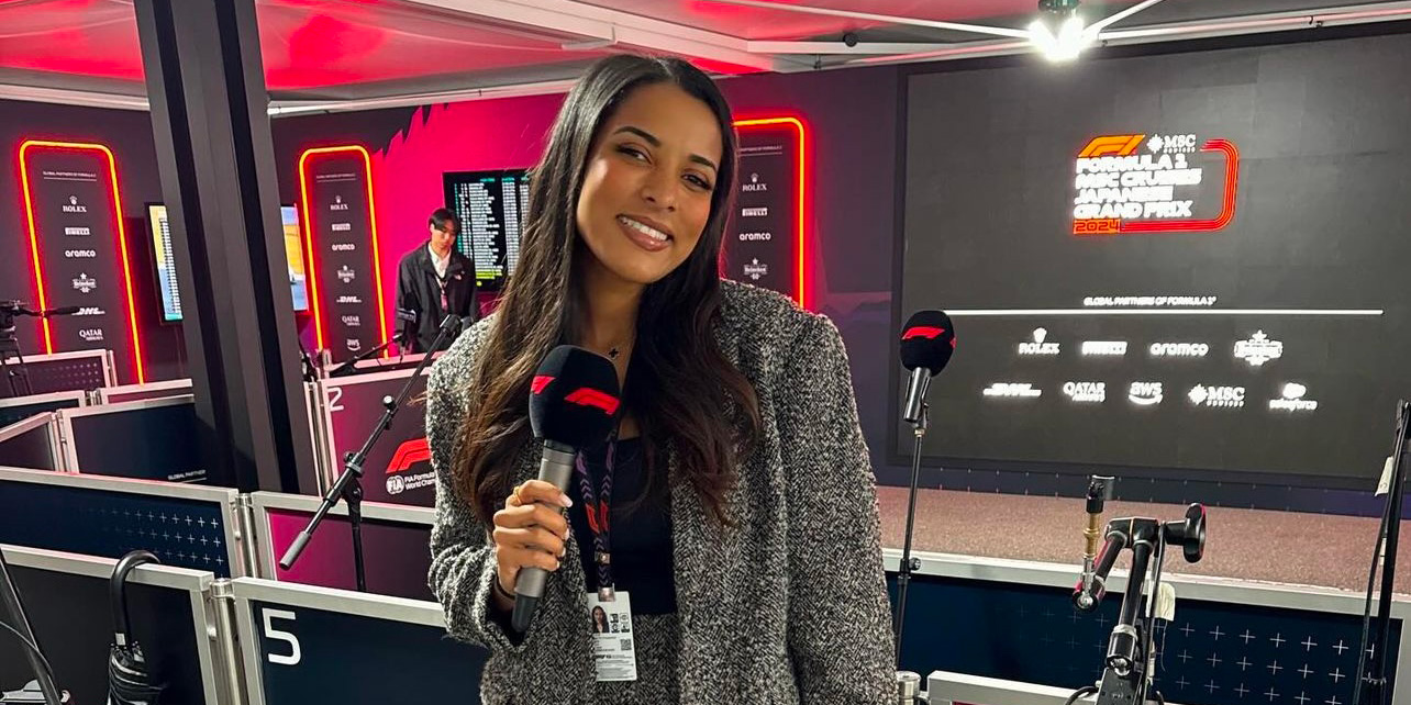 Ariana Bravo standing outside the F1 media pen, smiling at the camera, holding a microphone
