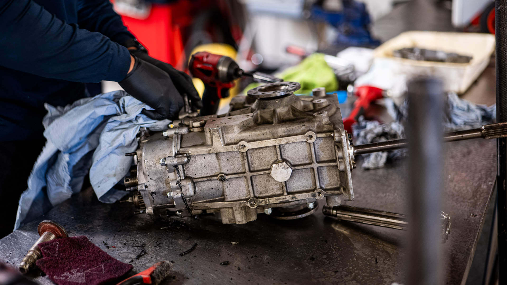 A mechanic works on a car engine part, cleaning it with a blue rag.