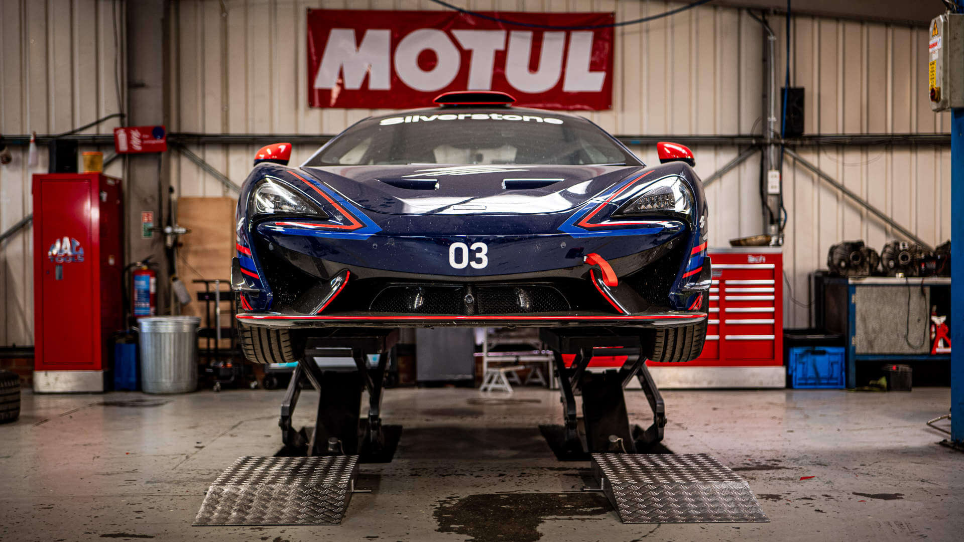 A McLaren 620R in Silverstone livery sits atop stands lifting it off the ground