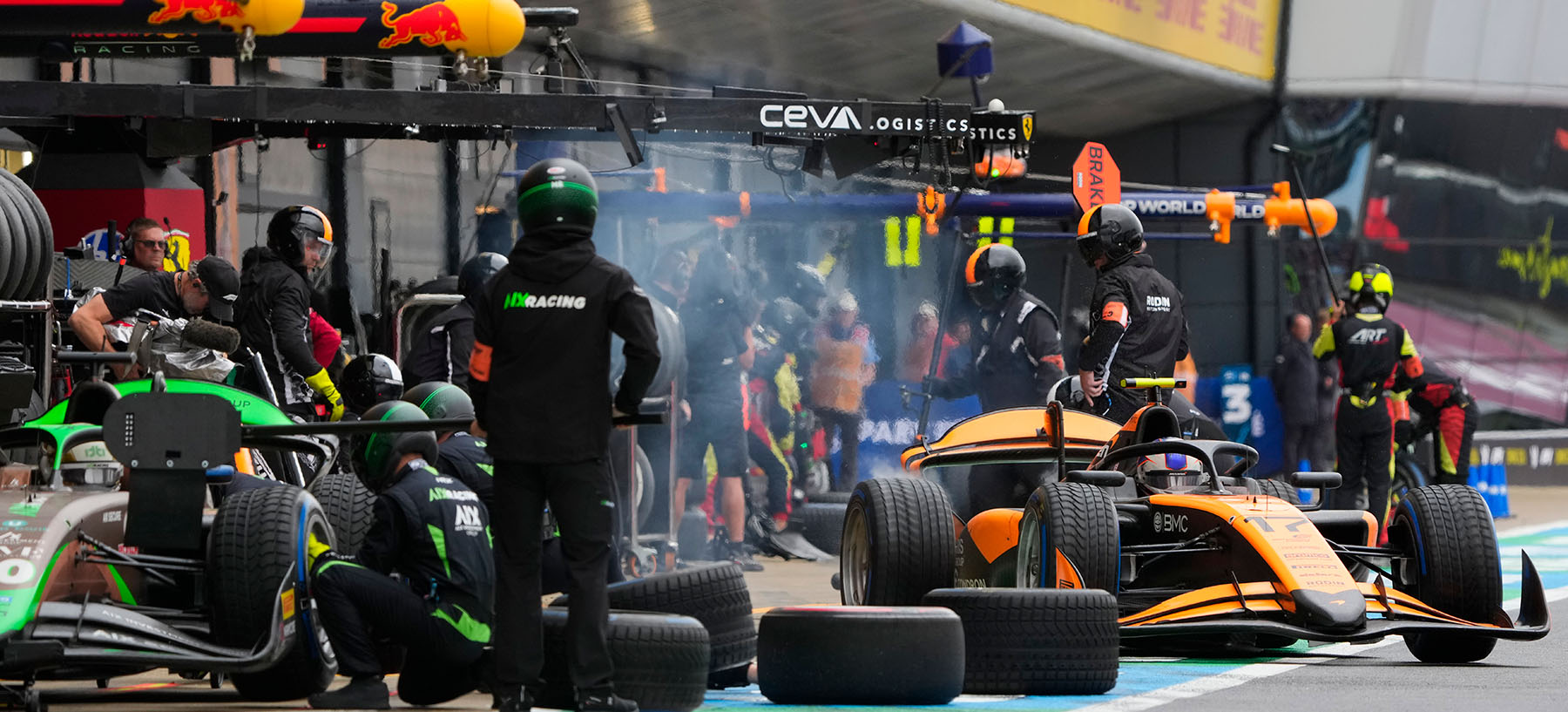 FIA F2 car in the pitlane at Silverstone. Orange McLaren liveried car enters the main pitlane after a pitstop for wet tyres 