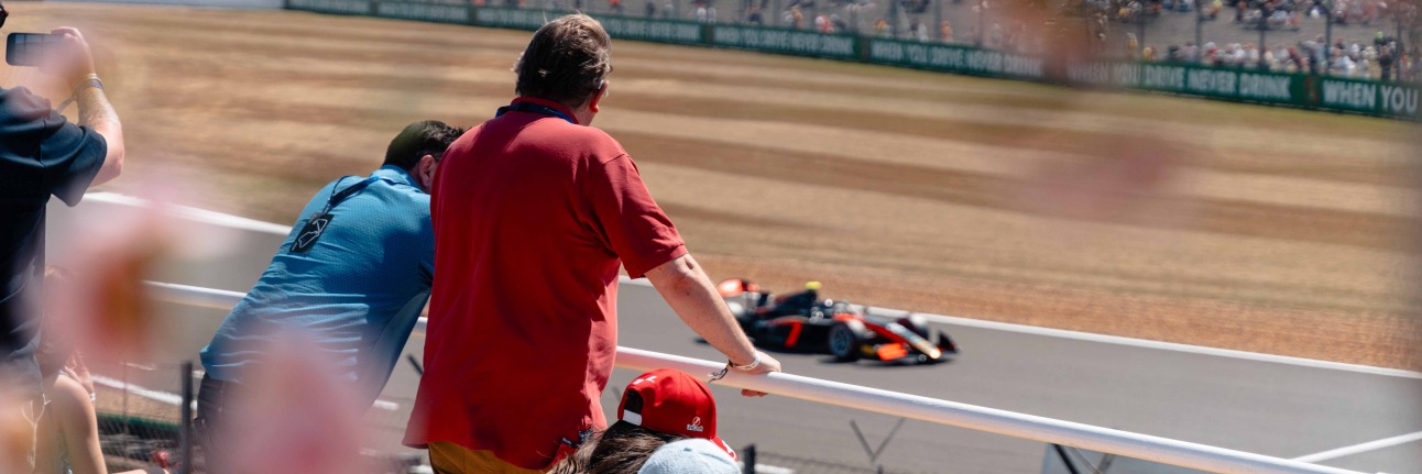 An F1 fan enjoying British Grand Prix Hospitality with an F2 car on track at Silverstone