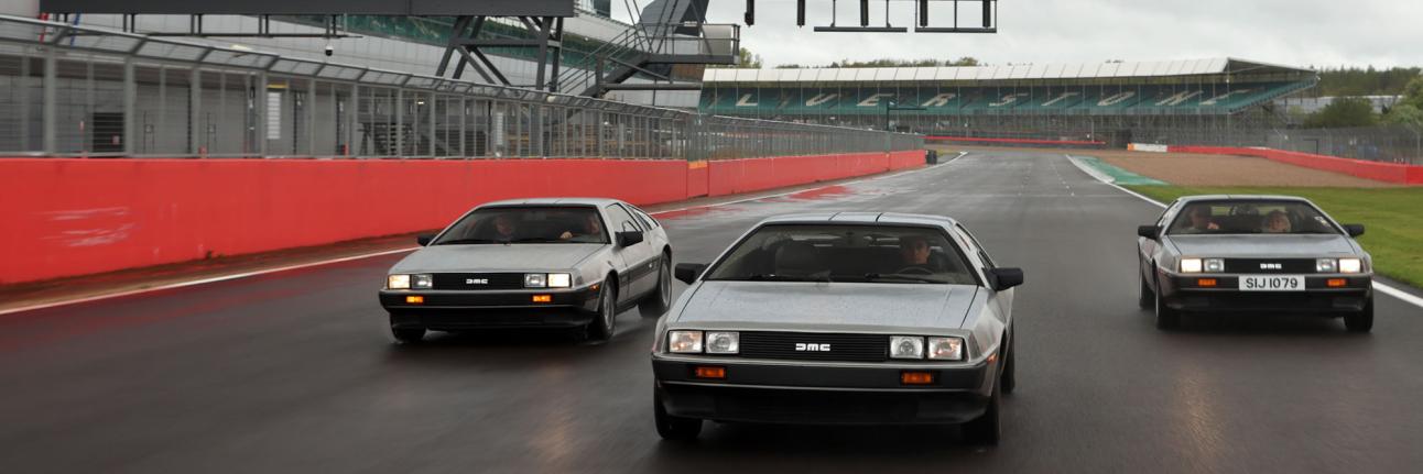 Three DeLoreans driving past the wing at Silverstone