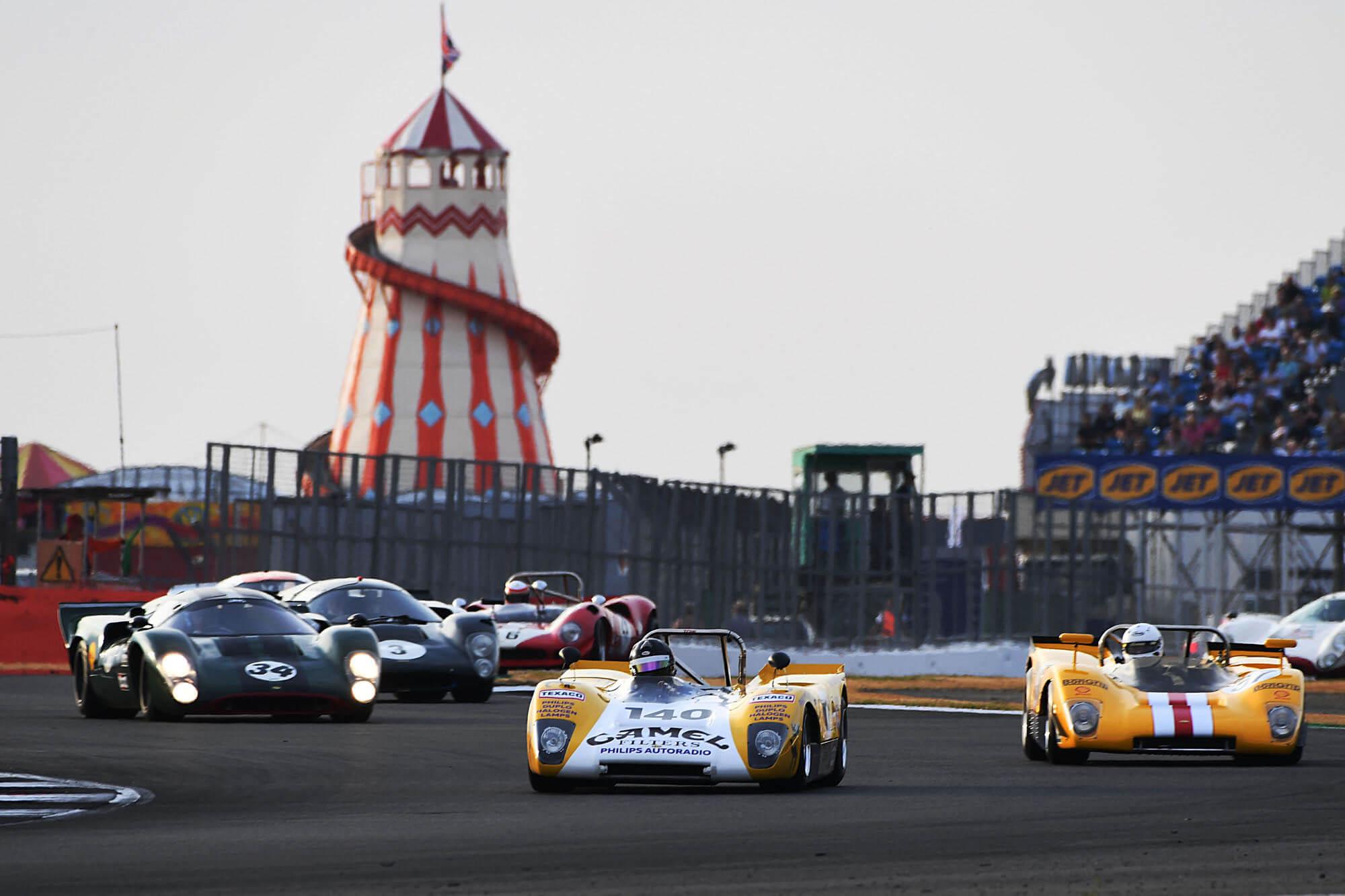 Six cars racing in the Masters Historic Sportscars grid at The Classic at Silverstone with the helter skelter in the background