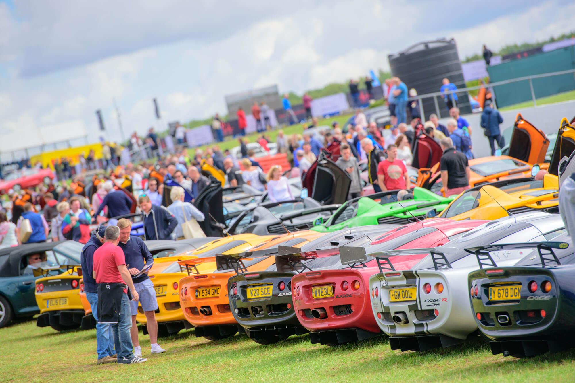 A line-up of brightly coloured classic cars displayed as part of a Car Club at The Classic at Silverstone and a crowd of people looking at the display