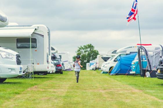 A child running away from the camera between two rows of tents and campervans in a camping field 