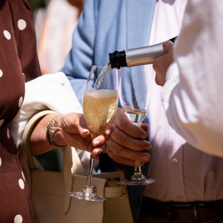 person pouring bottle of champagne into person's glass. just hands and obscured bottle visible