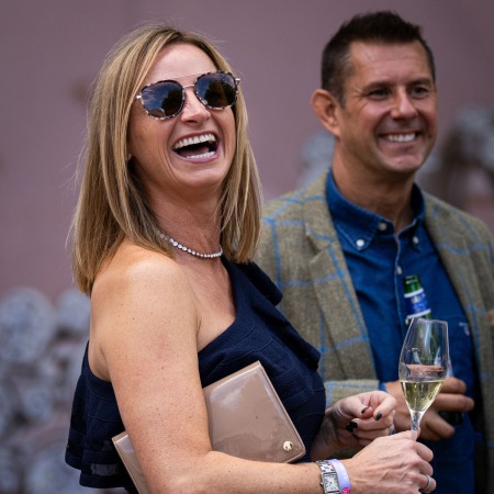 person smiling wearing sunglasses. clutching purse and a bottle of champagne