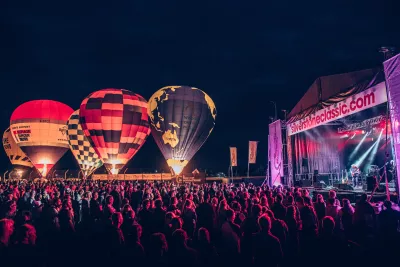A large crowd gathered in the evening in front of the concert stage at The Classic at Silverstone with hot air balloons lit up in the background